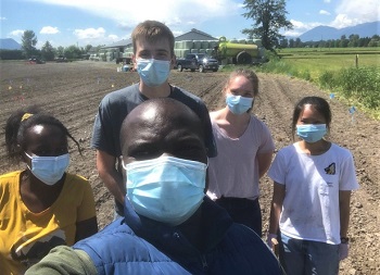 A selfie-style image of Dr. Messiga and four of his students in a field on a sunny day, getting ready for an experiment