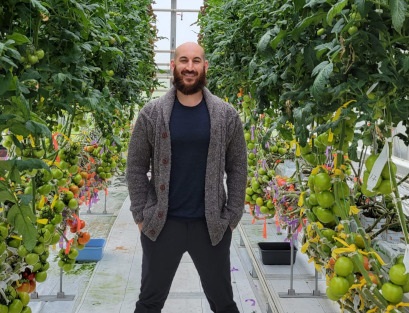 Dr. Jason Lanoue standing in a greenhouse between two rows of vertically-grown tomatoes.