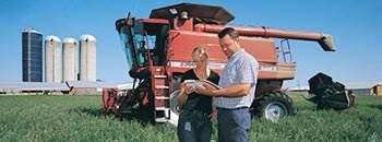 A man and a woman looking at a book in the middle of a farm.