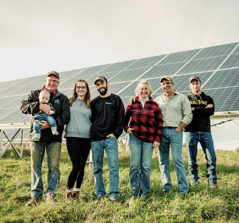 Nancy's father with her grandson in his arms, the mother of the child, Nancy's sons as well as she and her husband in front of a large solar panel.