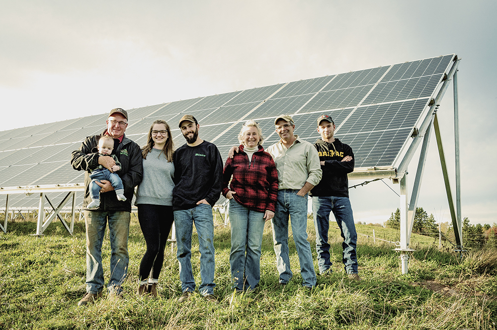 Nancy’s father with her grandson in his arms, the mother of the child, Nancy’s sons as well as she and her husband in front of a large solar panel.