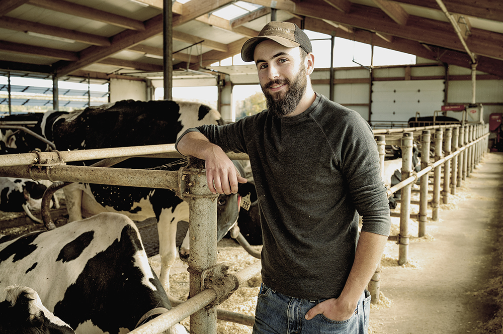 One of Nancy's sons standing beside cows in a barn.