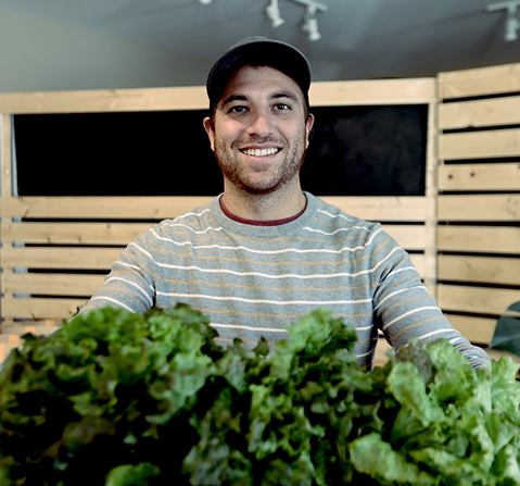 Tarek smiling and holding a large basket of fresh lettuce