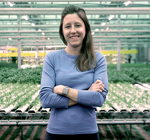 Lauren smiling with her arms crossed, in front of thousands of young shoots, in a large greenhouse
