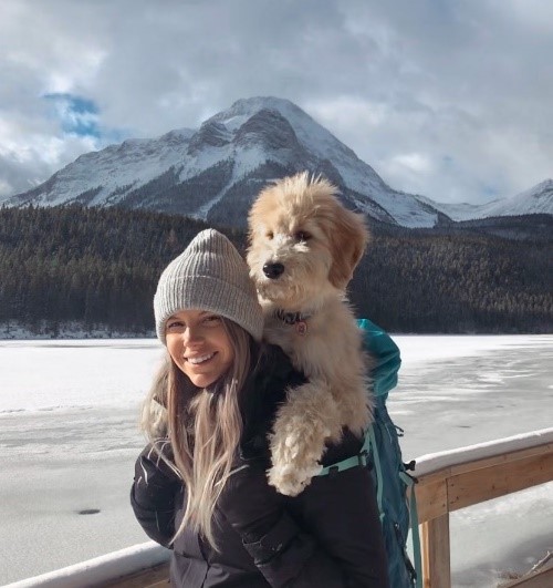 Photographie de Katelyn Lutes, portant son chien sur son dos, avec un paysage de montagne en arrière-plan