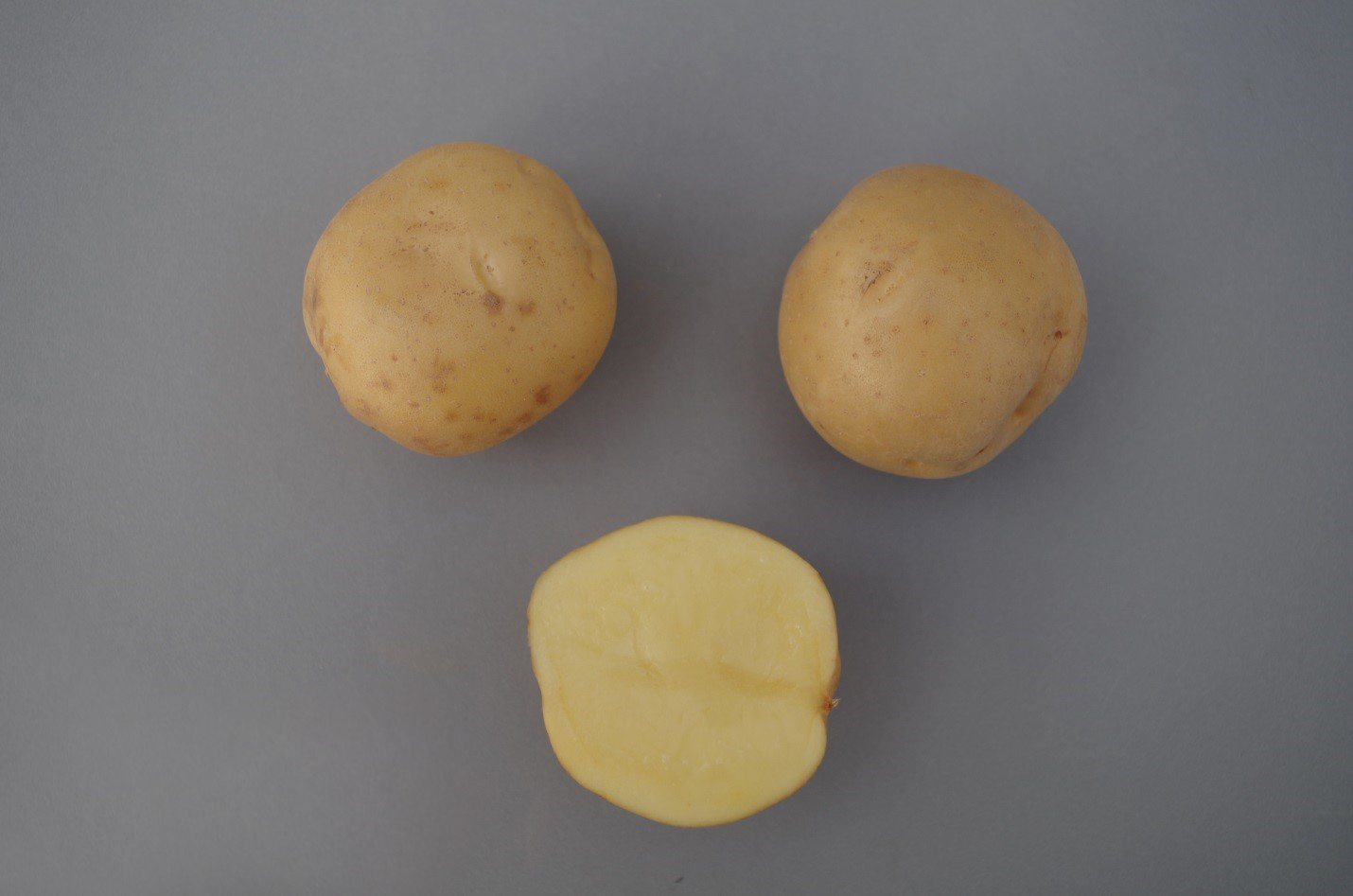Deux pommes de terre entières et une pomme de terre coupée en deux.