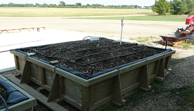 An up-close photo of a biobed in early production showing a wooden square enclosure filled with biomix and black drip irrigation tubes across the top.