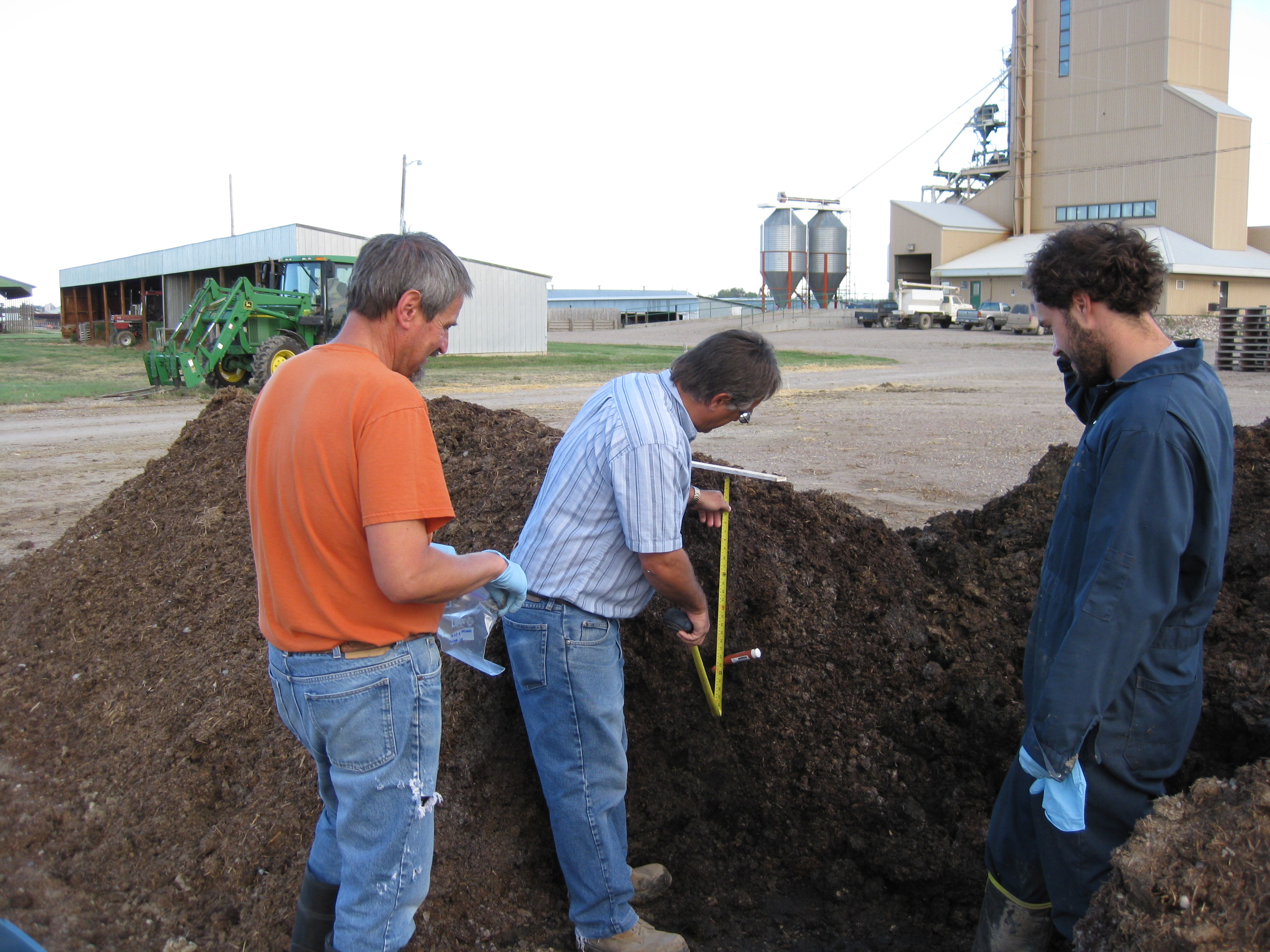 Three researchers examining compost outdoors.