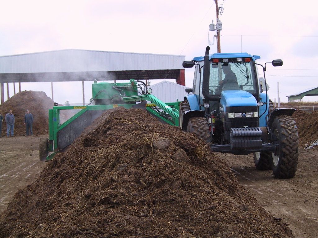 A blue tractor turning over manure.