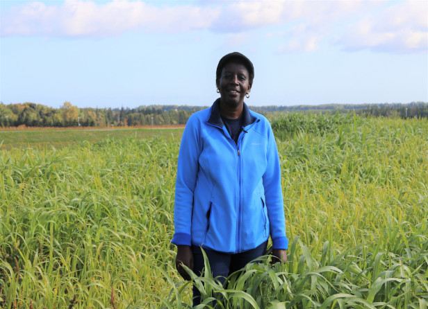 A research scientist smiling and standing outdoors in a field of crops.