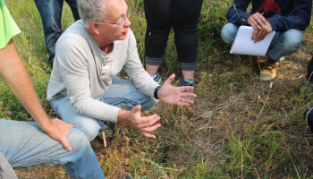Dr. Kevin Floate crouches in a pasture with students grouped around him