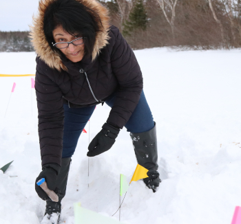 Une scientifique debout dans la neige montre un tube de plastique rempli de taupins