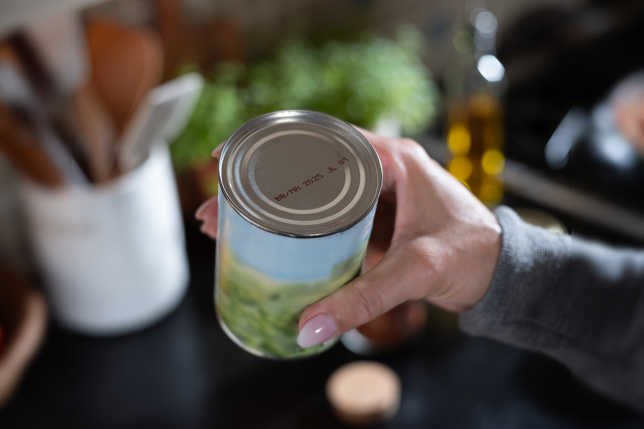 A hand holding a can of food with a best before date