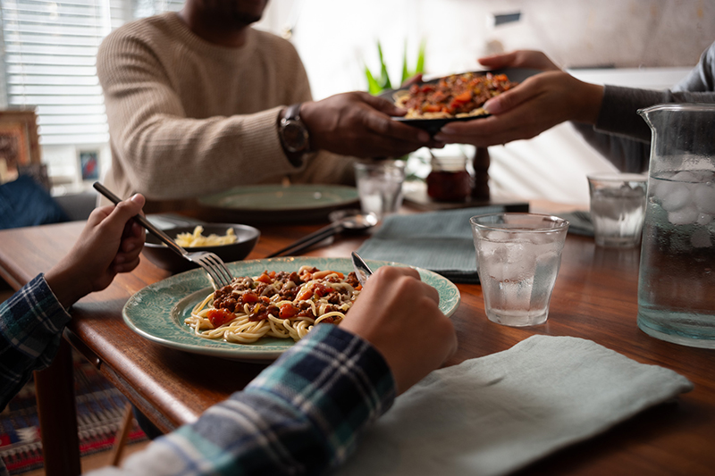 Gros plan sur une famille qui se partage des assiettes de spaghettis à table lors d'un repas. 