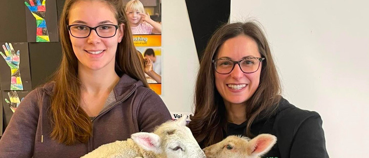 Two women holding baby lambs.