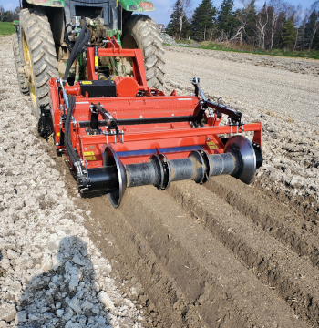 A tractor pulling the stone burier and bed shaper reverse rotary tiller equipment behind it in a field.