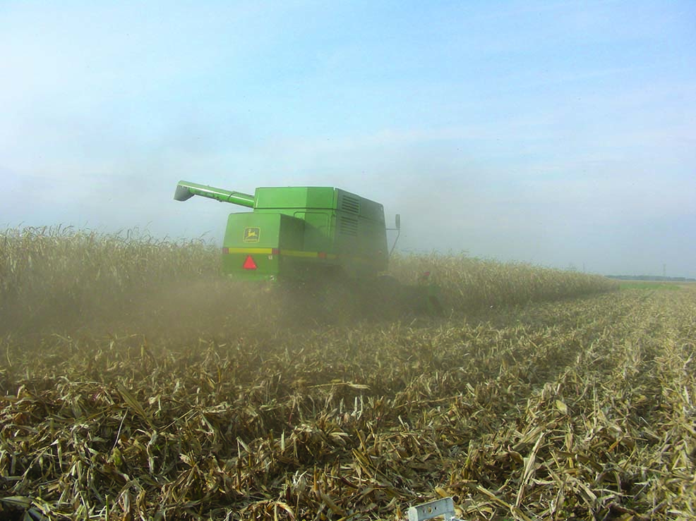 Image displays a combine harvester moving through the field and the resulting dust in the air.