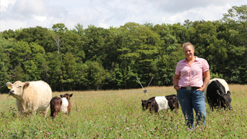 Un fermier debout dans un champ avec des vaches et une clôture en arrière-plan