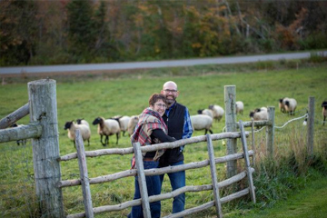Deux personnes se tenant près d'une clôture avec des moutons en arrière-plan.